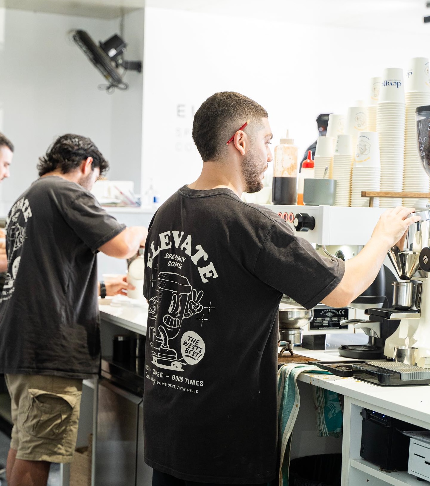Elevate black shirt worn by barista behind the coffee machine